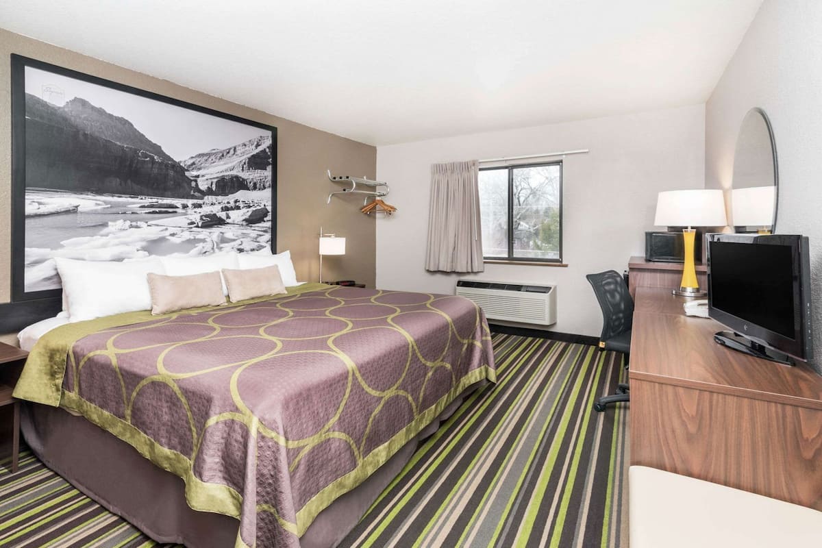 Quarto de hotel com uma cama, uma escrivaninha com televisão, uma janela e uma moldura grande na parede.