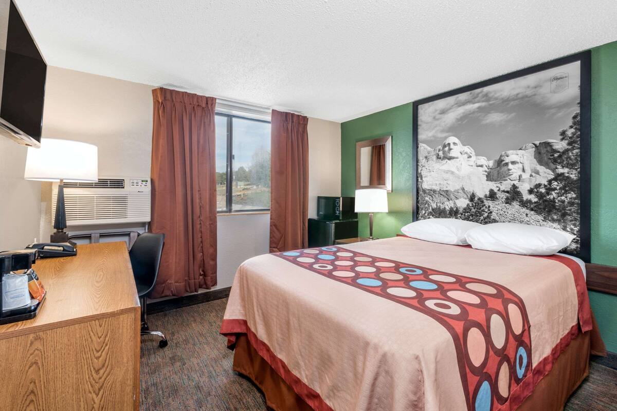 A hotel room with a bed, desk, chair, and a large window.