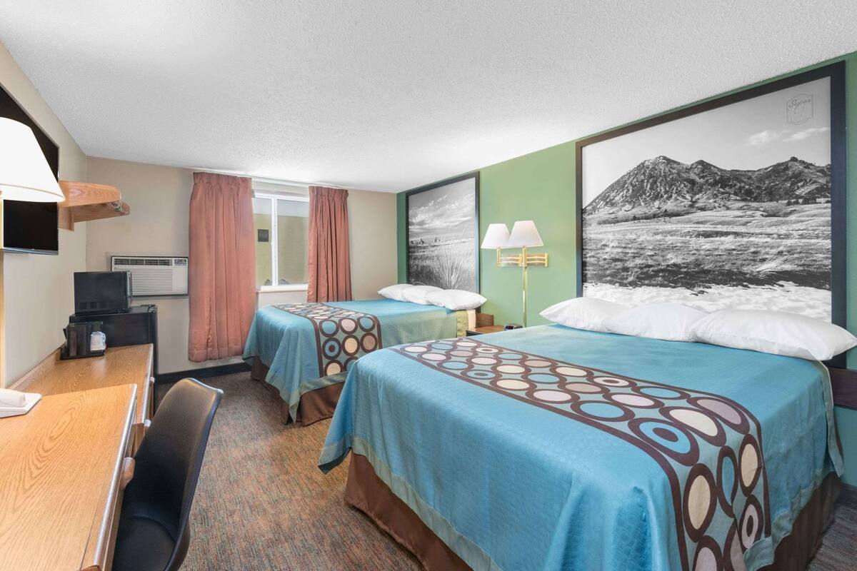 A hotel room with two beds, a desk, a television, and a large window with a mountain view.