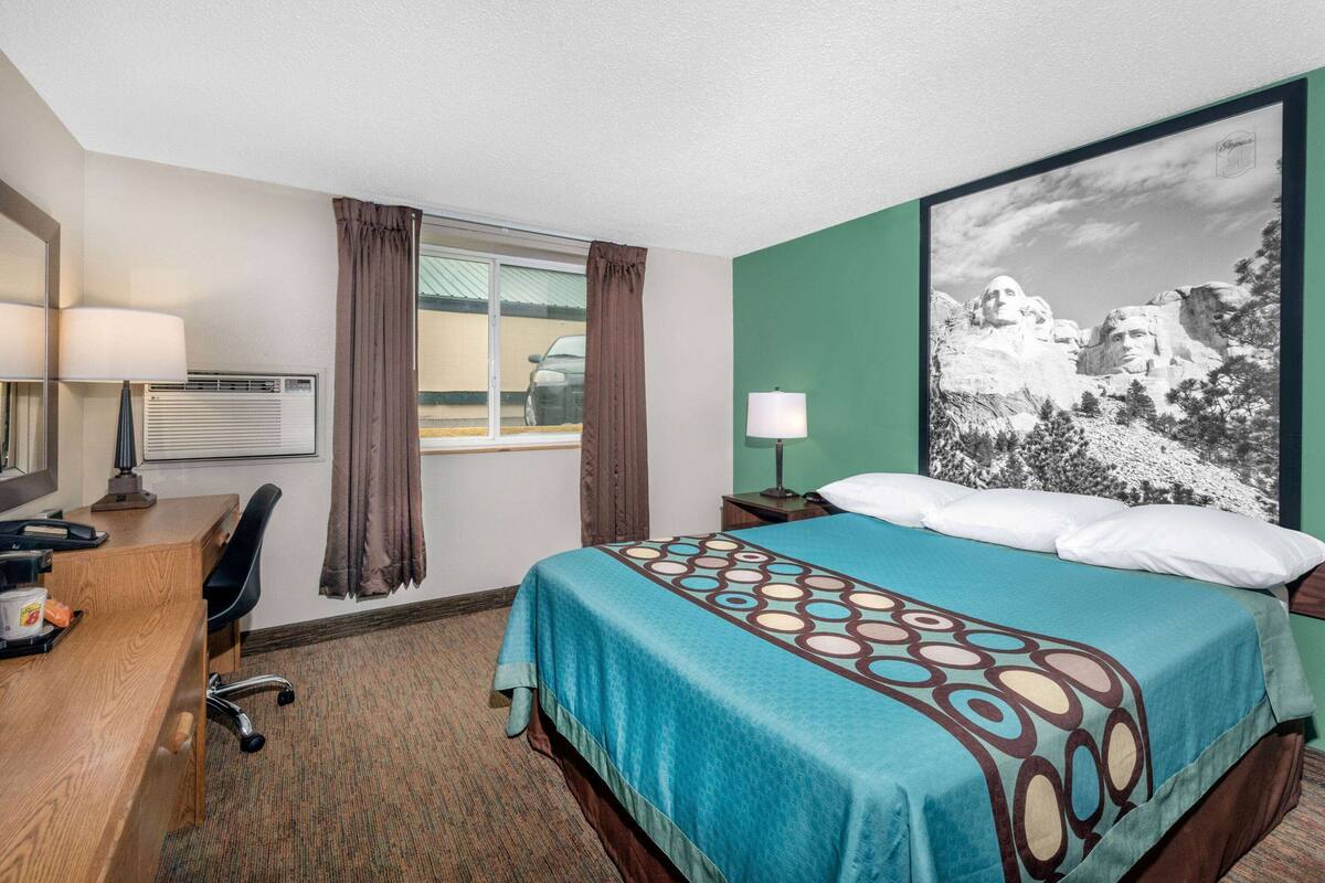 A hotel room with a bed, desk, chair, and a large window.