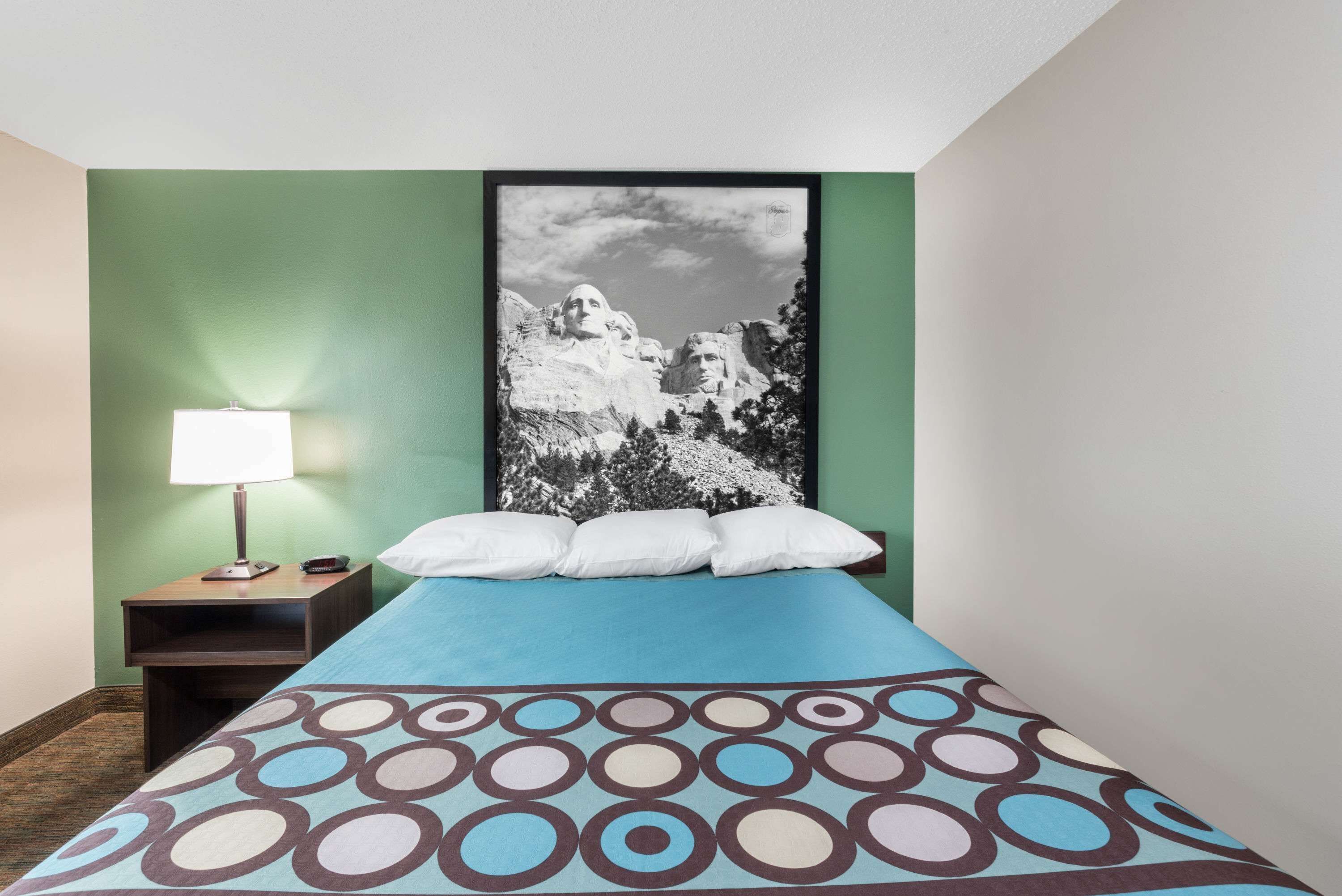 A hotel room with a bed, a nightstand with a lamp, and a framed picture of a mountain on the wall.