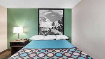 A hotel room with a bed, a nightstand with a lamp, and a framed picture of a mountain on the wall.