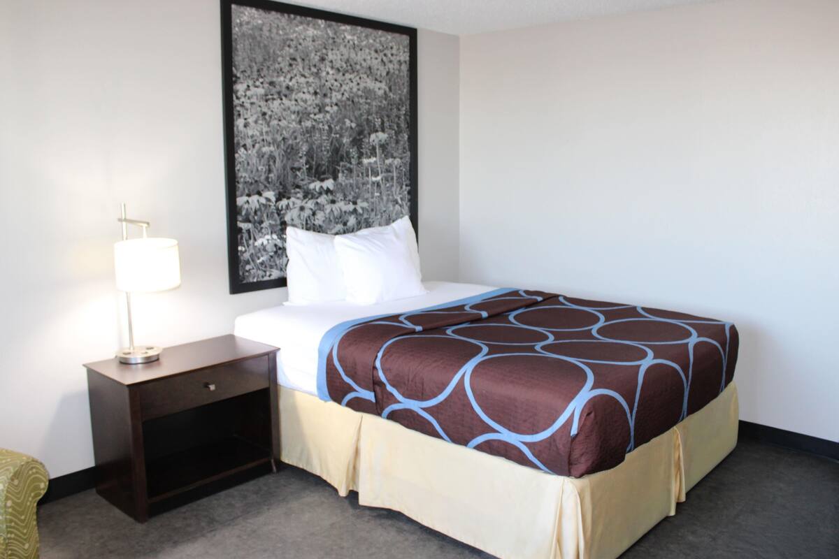 A hotel room with a bed, a nightstand, a lamp, and a large framed picture on the wall.