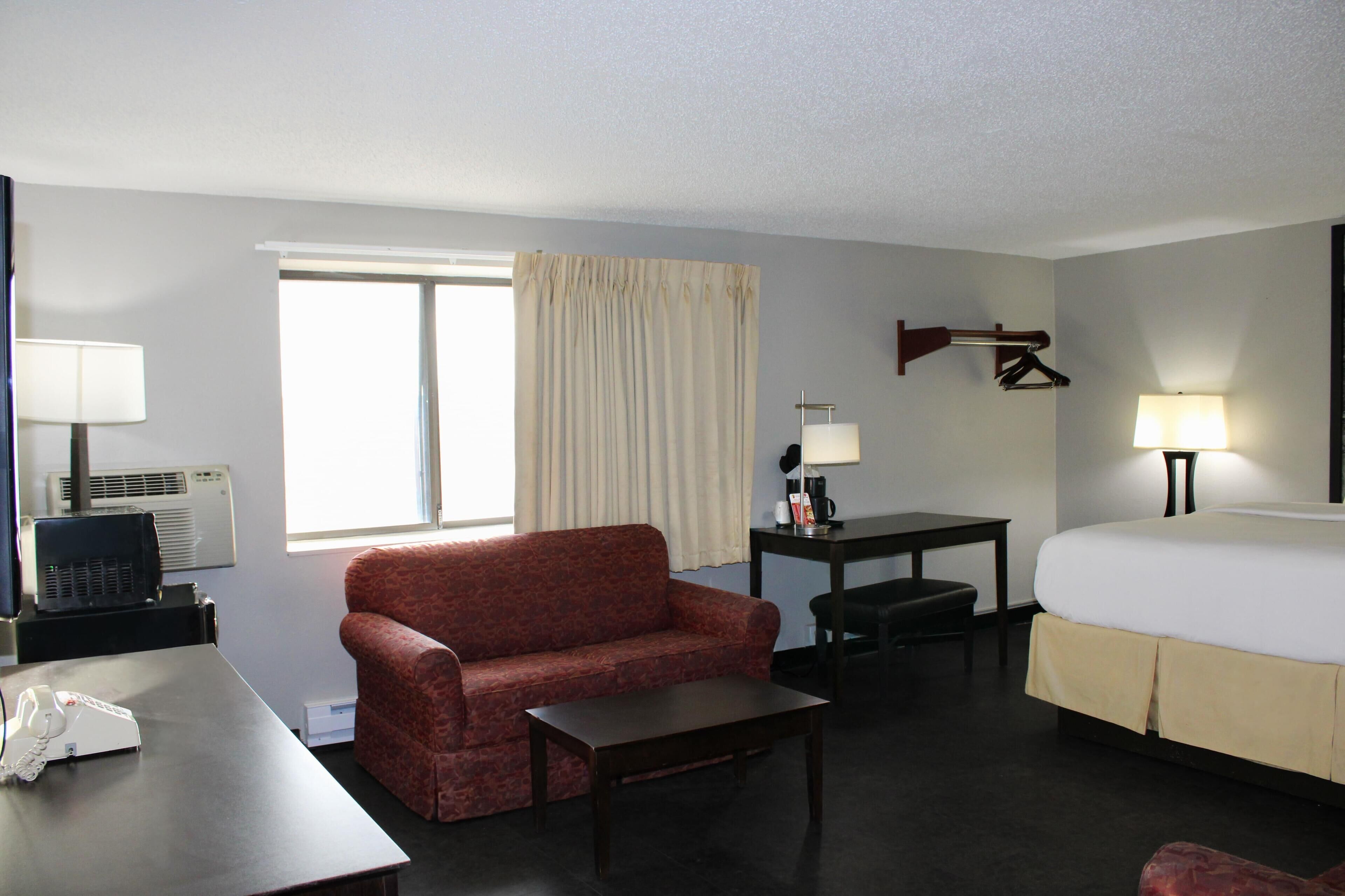 A hotel room with a bed, a sofa, a desk, a lamp, and a window with curtains.