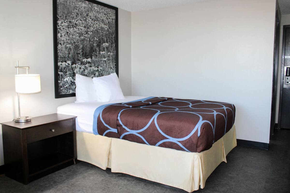 A hotel room with a bed, a nightstand, a lamp, and a large black and white photograph on the wall.