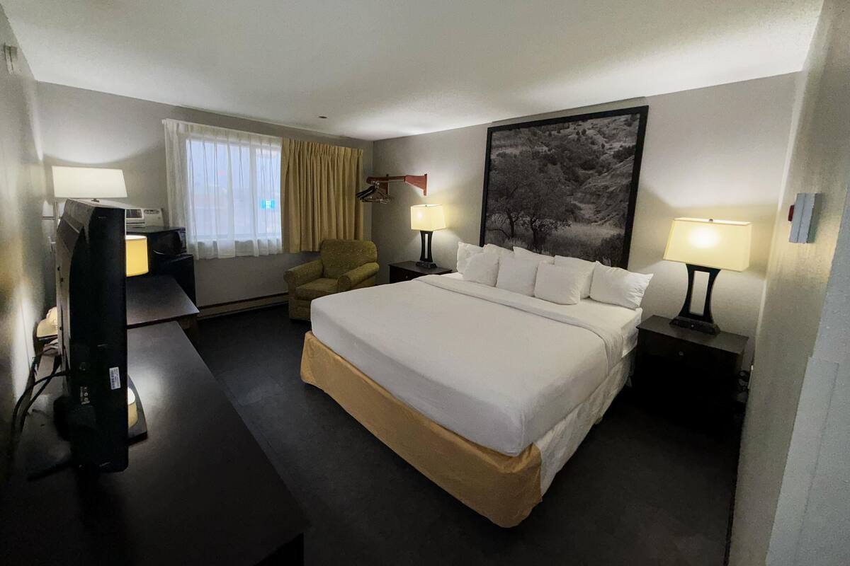 A hotel room with a large bed, two bedside lamps, a chair, a desk with a computer, and a television.