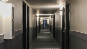 Un largo pasillo de hotel, estrecho, con puertas a ambos lados, piso cubierto de alfombra e iluminación en el techo.