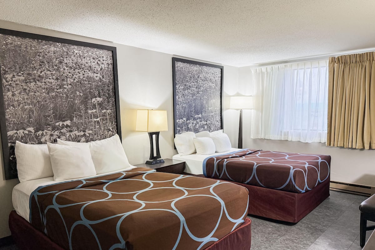 A hotel room with two beds, a desk, and a large window with curtains.