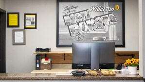 Un área de recepción con un letrero de bienvenida enmarcado, una computadora de escritorio, una impresora y una estación de café.
