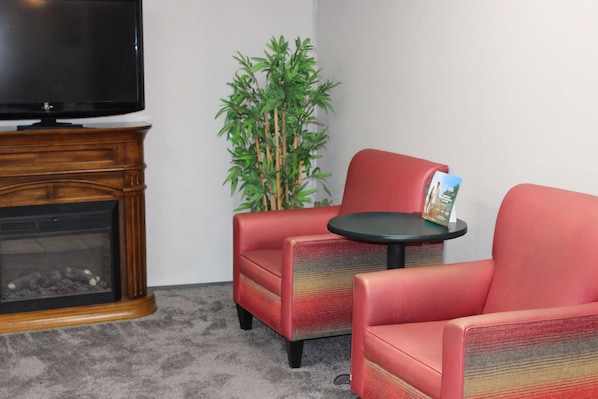A corner room with a fireplace, a television, two red armchairs, a small round table, and a green plant.