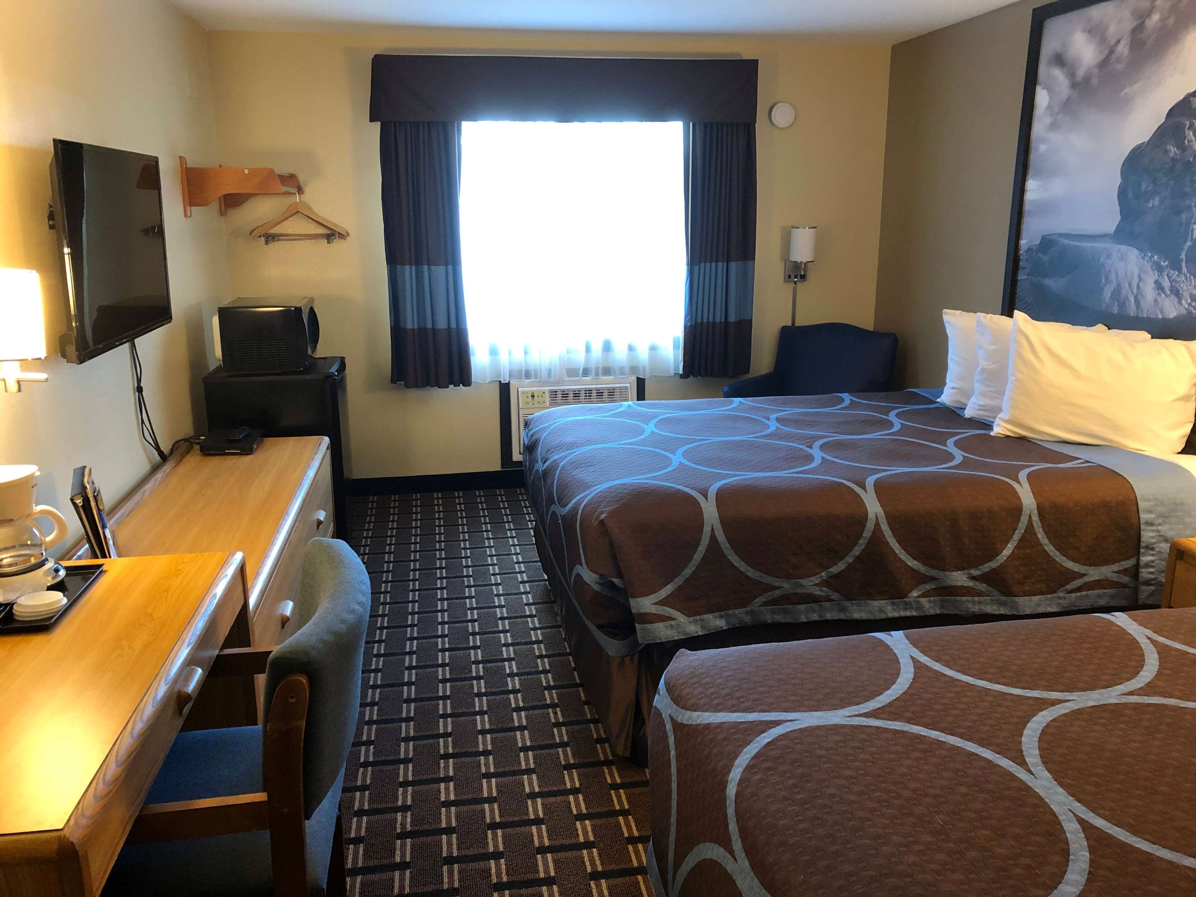 Quarto de hotel com cama, duas mesas de cabeceira, escrivaninha com cadeira, televisão e janela com cortinas.