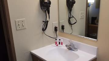 Casa de banho com uma pia branca, espelho, secador de cabelo e um cesto de lixo.