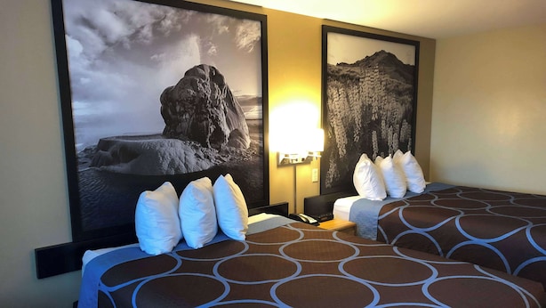 A hotel room with two beds, each with a patterned bedspread and white pillows. There are framed pictures on the wall, a bedside lamp, and a flat-screen TV. - Super 8 by Wyndham Carson City/Lake Tahoe (Carson City)
