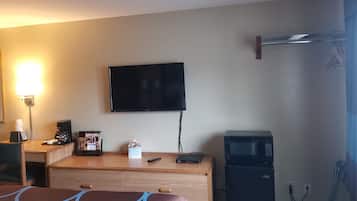 A hotel room with a bed, a desk with a coffee maker, a microwave, and a flat-screen TV mounted on the wall.