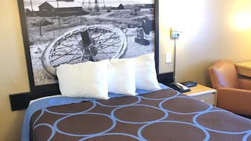 A hotel room with a large bed, a chair, a desk with a phone, and a wall-mounted picture of a mining scene.