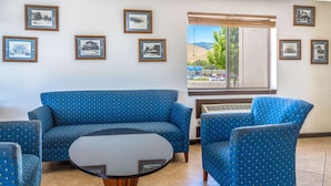 A room with a blue sofa, matching armchair, and a small round table. There are framed pictures on the wall and a window with a view of mountains and trees. - Super 8 by Wyndham Carson City/Lake Tahoe (Carson City)
