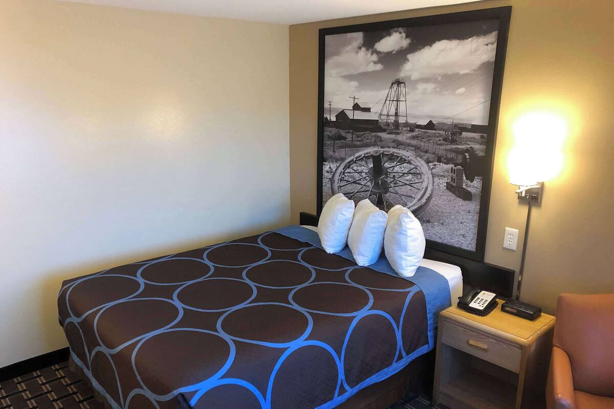 Ein Hotelzimmer mit einem Bett, einem Nachttisch mit Telefon, einem Sessel und einer Wandlampe.