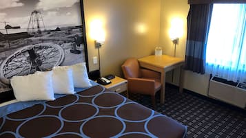 A hotel room with a bed, a desk, a chair, a lamp, and a window with curtains.