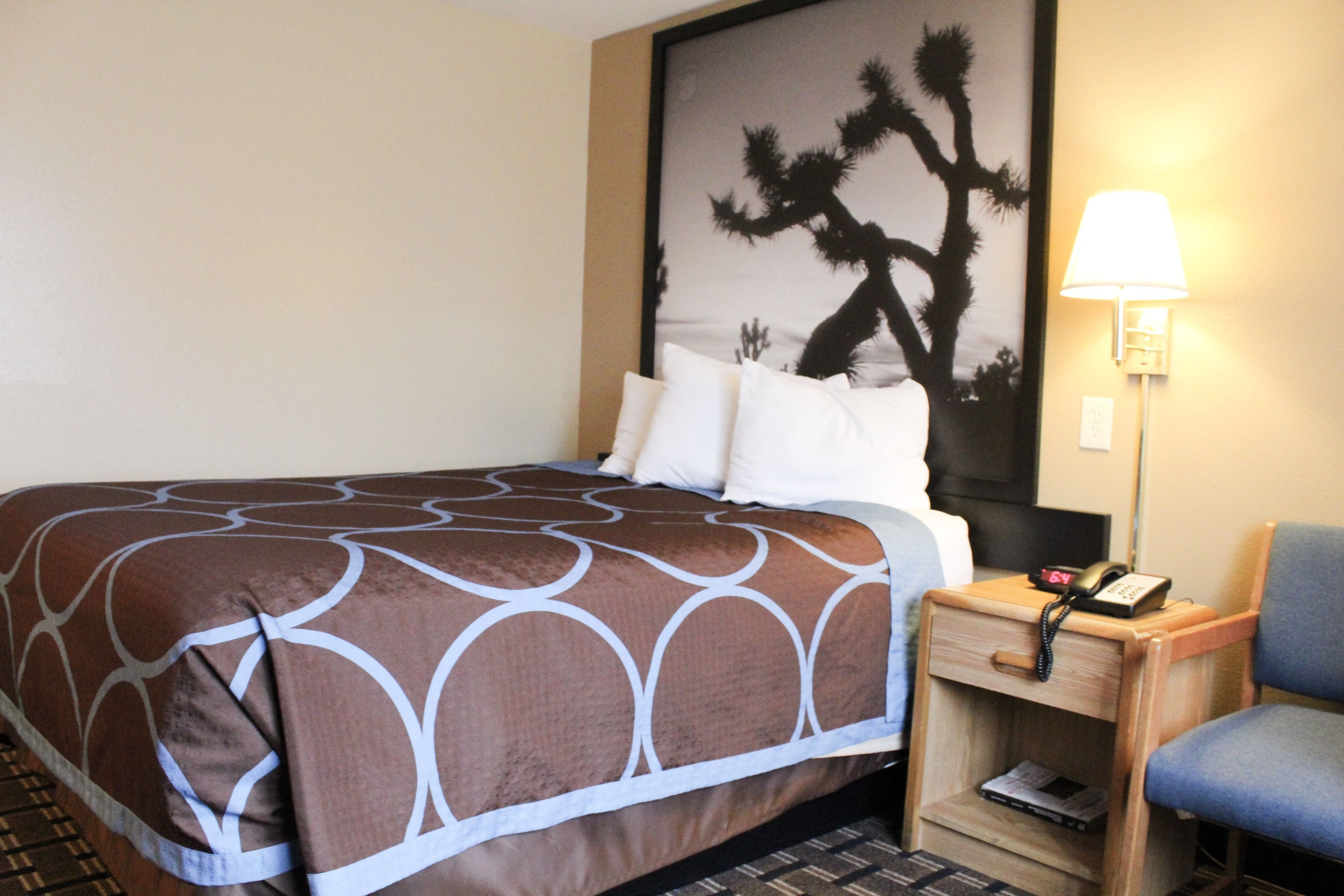 A hotel room with a bed, a nightstand with a lamp, and a chair.