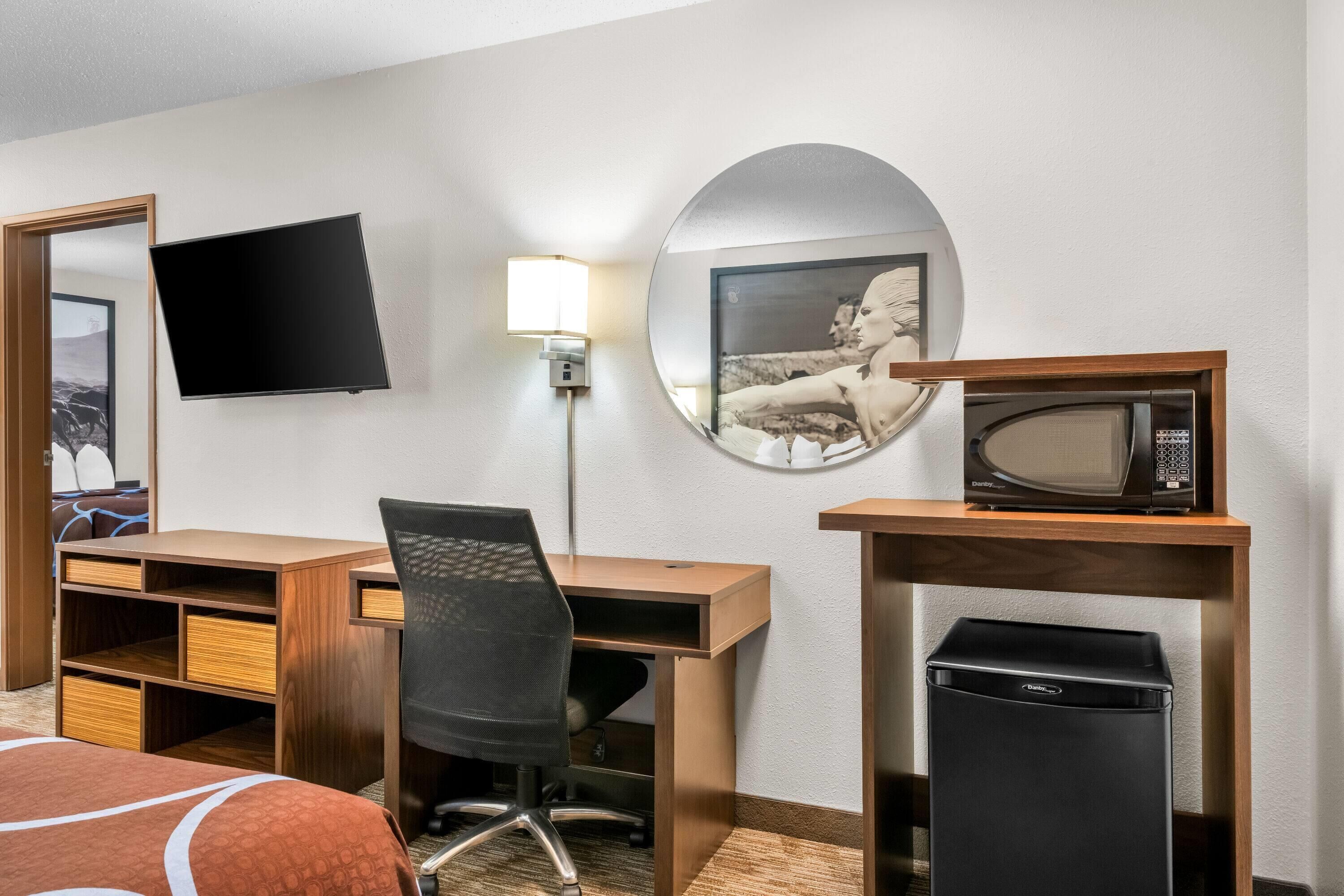 Habitación de hotel con cama, escritorio con silla, televisor de pantalla plana, microondas y cubo de basura.