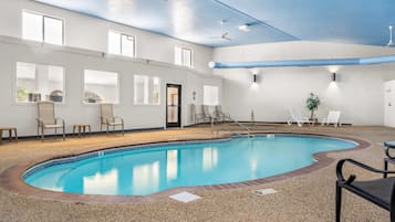 An indoor swimming pool with a pebble floor, surrounded by lounge chairs and a ceiling fan.