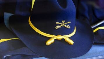 A navy blue hat with a gold emblem and ribbon, displayed on a surface.