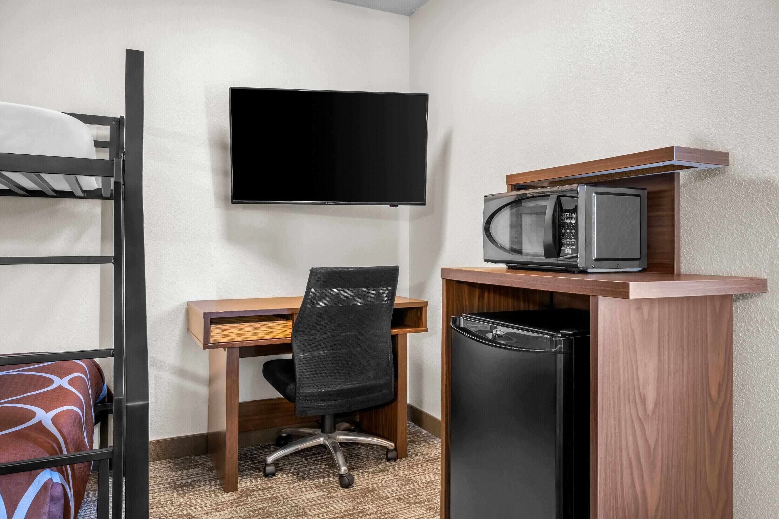 Une chambre d’hôtel compacte comprenant un lit superposé, un bureau avec une chaise, une télévision, un four à micro-ondes et un réfrigérateur.