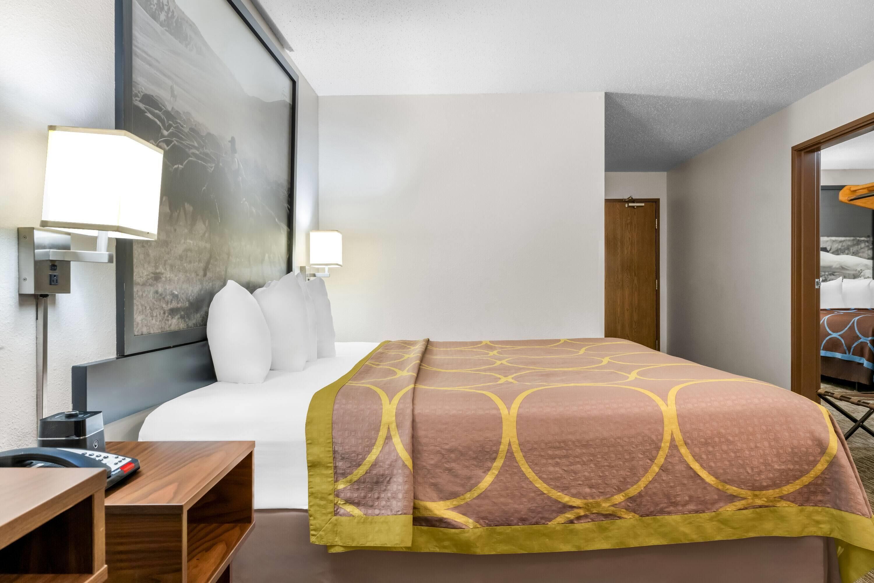 Una habitación de hotel con una cama grande, lámparas de noche, un escritorio y un cuadro grande en la pared.