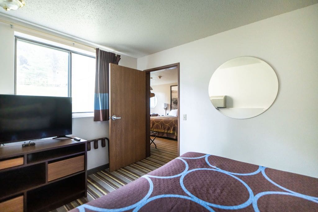Una camera d'albergo con un letto, una televisione su un mobile in legno, uno specchio a parete e una finestra con tende.