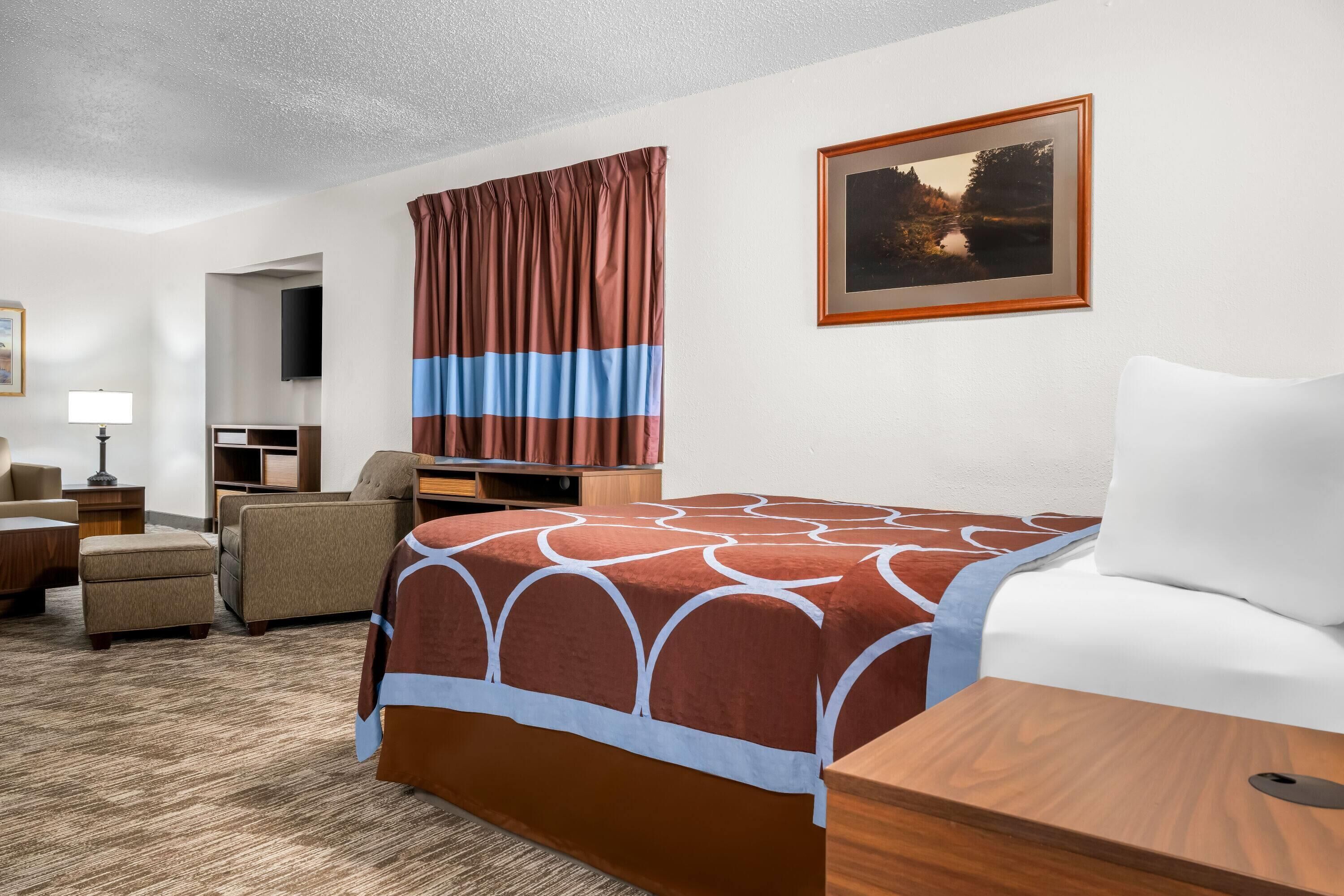 Habitación de hotel con cama, escritorio, silla, lámpara y un cuadro en la pared.