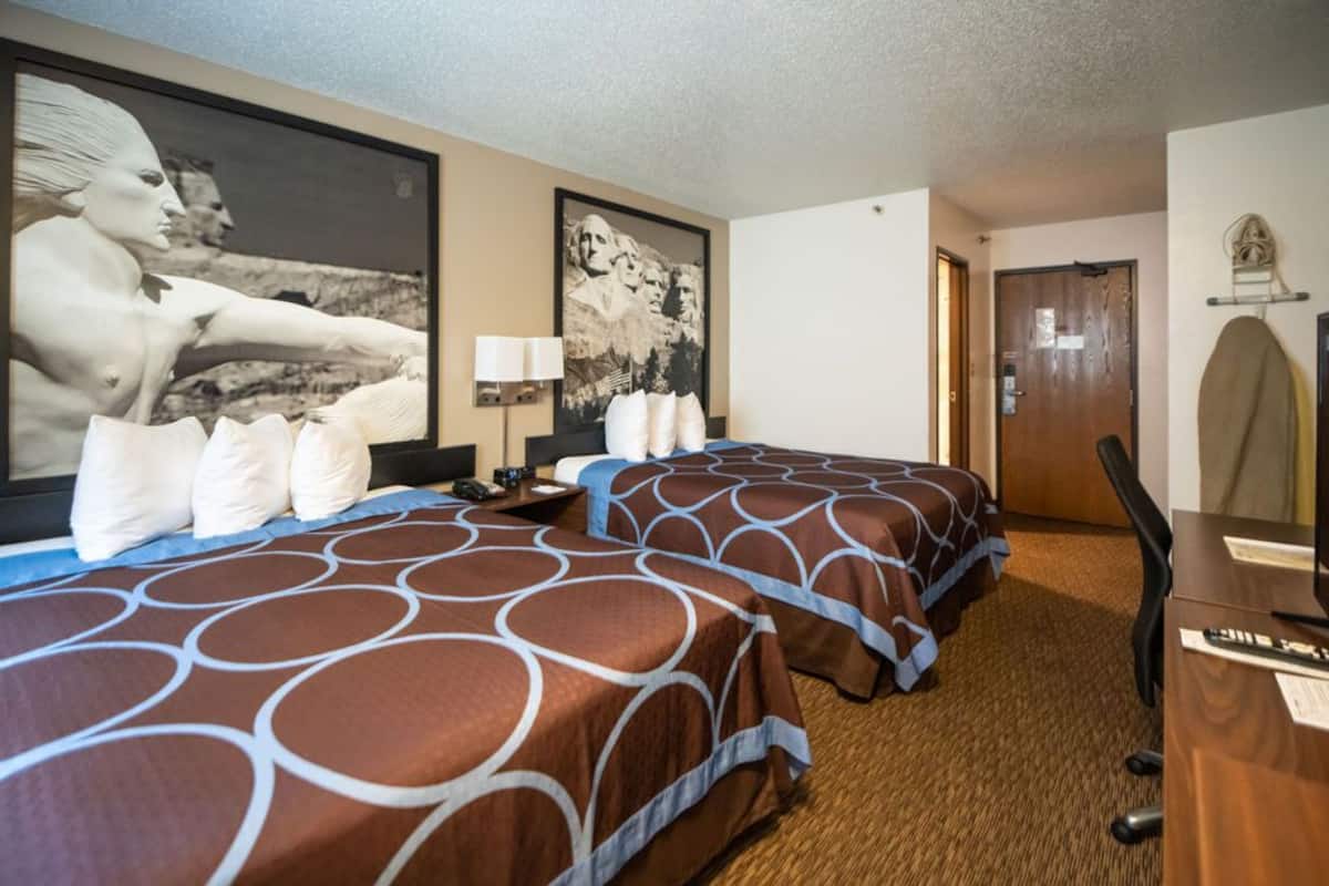 Een hotelkamer met twee bedden, een bureau, een stoel, een lamp en een deur.