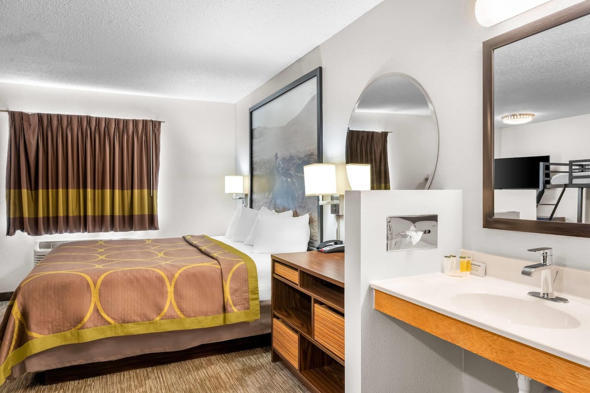 Een hotelkamer met een bed, een nachtkastje met een lamp, een grote spiegel en een badkamer met een wastafel en spiegel.
