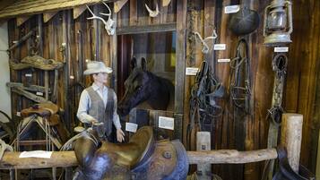 Une exposition de musée présentant une statue d’un cow-boy à cheval, ainsi que divers objets historiques, tels que des selles, des brides et une lanterne.
