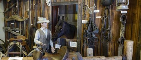 Une exposition de musée présentant une statue d’un cow-boy à cheval, ainsi que divers objets historiques, tels que des selles, des brides et une lanterne.