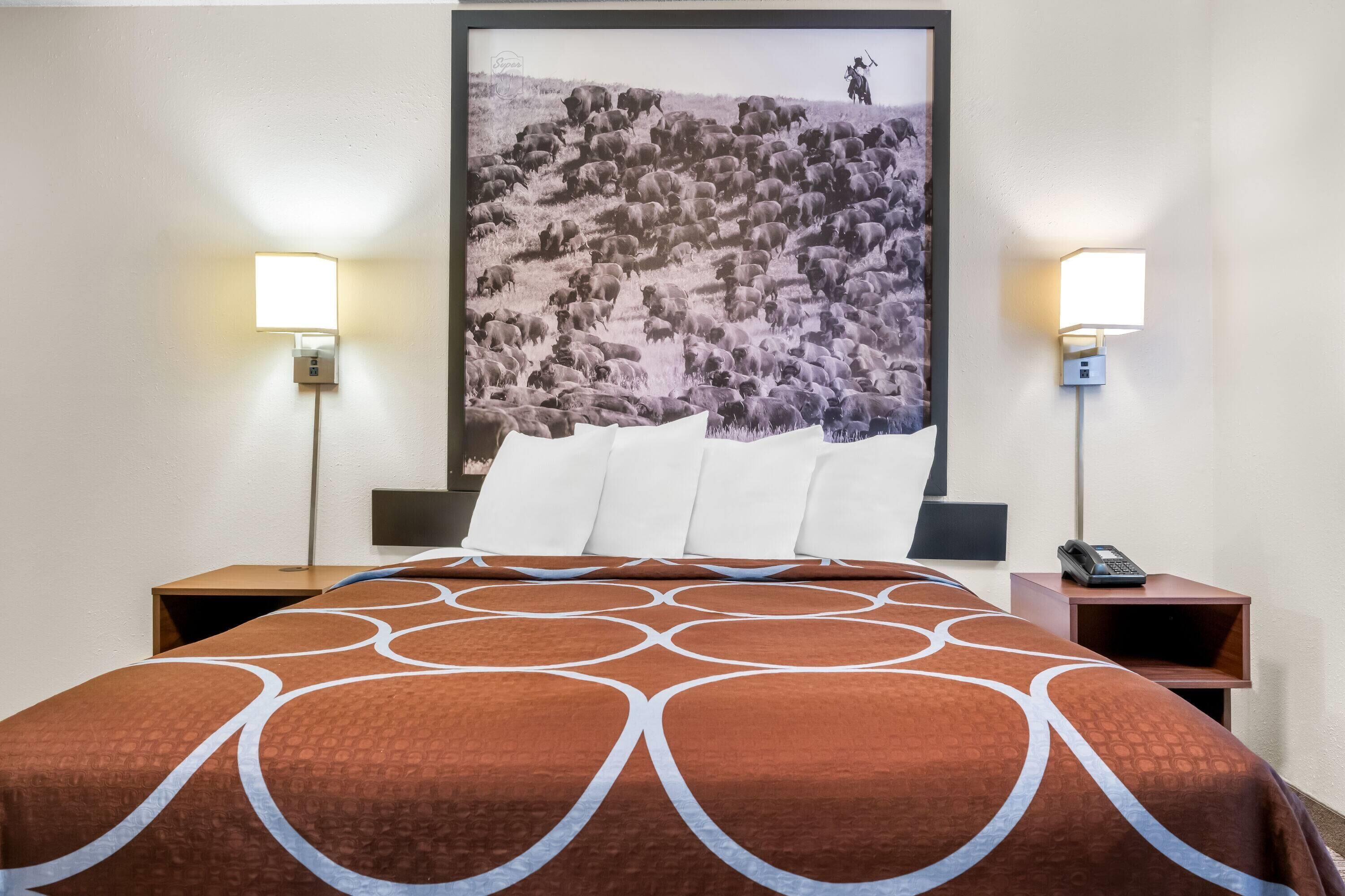 Hotellihuone, jossa on suuri sänky, kaksi yöpöytää, yölamppu ja seinään kiinnitetty valaisin.