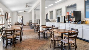 Un grand espace dédié à la salle à manger, avec plusieurs tables et chaises, un comptoir de cuisine équipé d’appareils électroménagers et de grandes fenêtres qui laissent entrer la lumière naturelle.