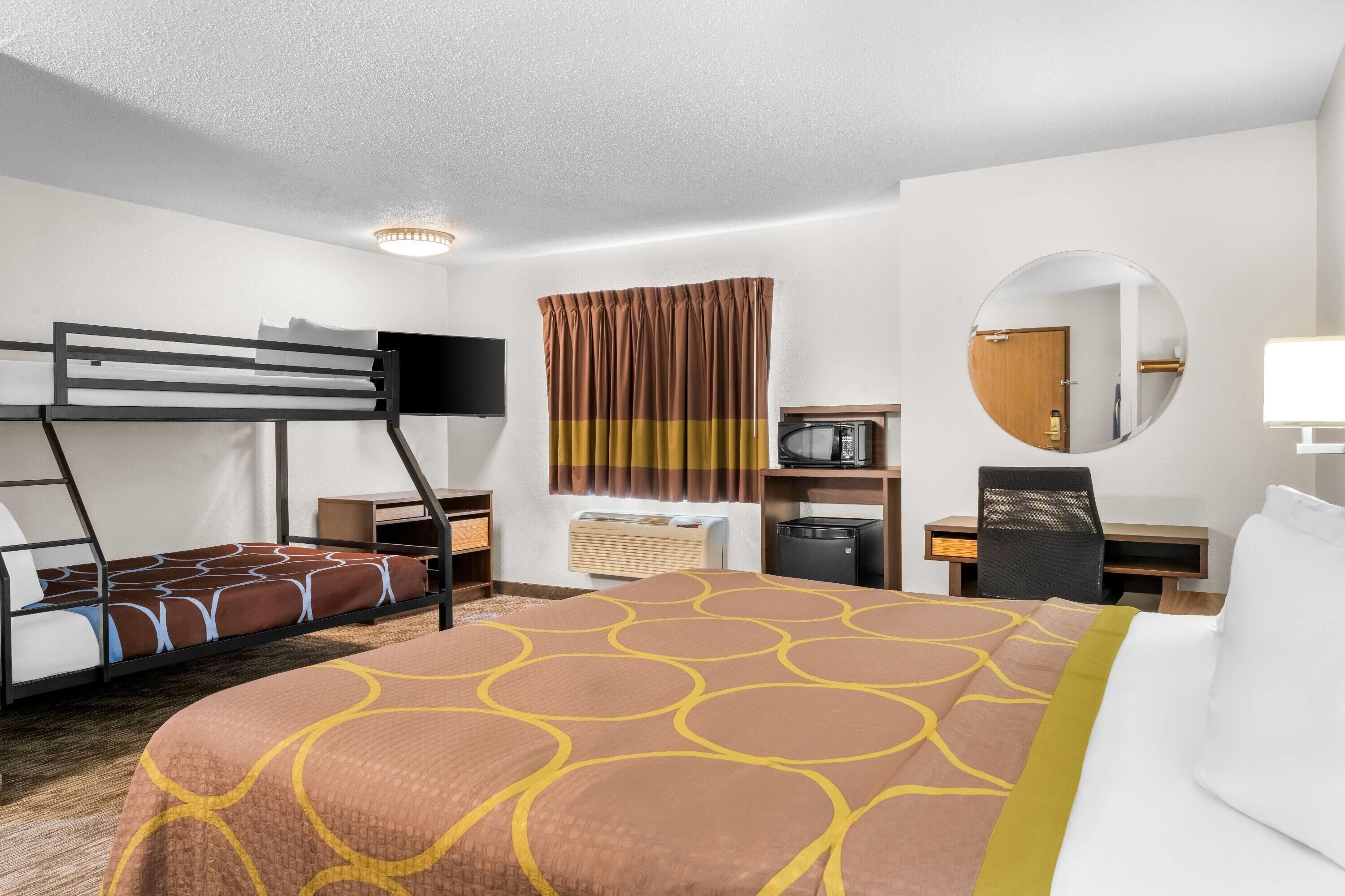 Habitación de hotel con literas, un escritorio, una silla, un espejo redondo, un televisor y un microondas.