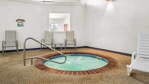 Une piscine intérieure bordée de bois, avec un escalier en métal et une pancarte indiquant « Bienvenue à la piscine ». On y trouve des chaises longues et un luminaire fixé au mur.
