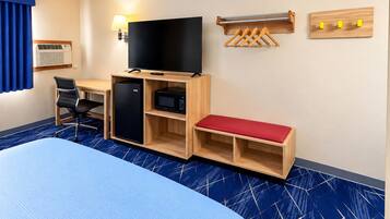 A hotel room with a bed, desk, chair, refrigerator, microwave, television, and a wall-mounted coat rack.
