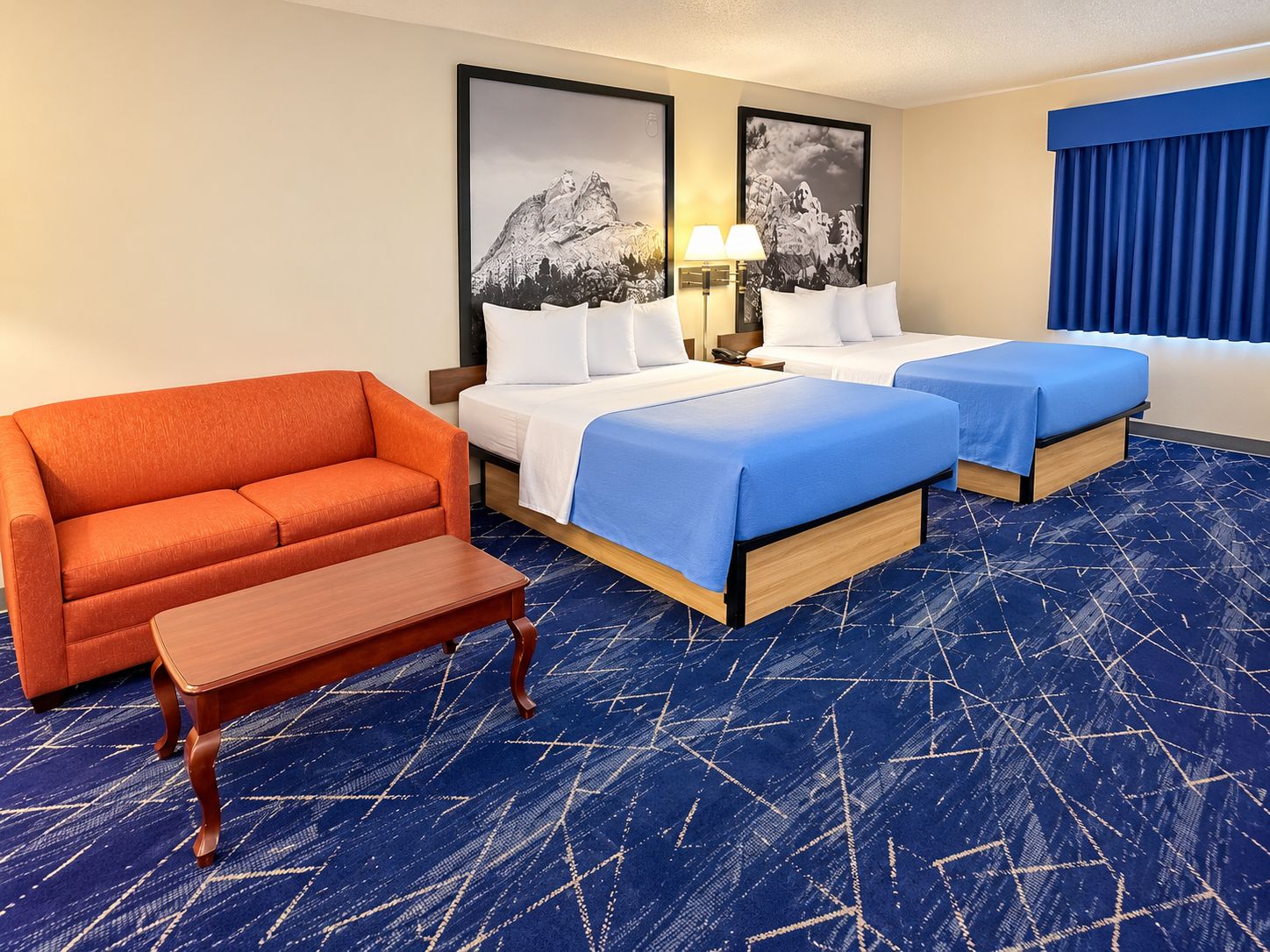 Habitación de hotel con dos camas, un sofá, una mesita y dos lámparas fijadas a la pared.