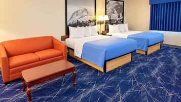 Habitación de hotel con dos camas, un sofá, una mesita y dos lámparas fijadas a la pared.
