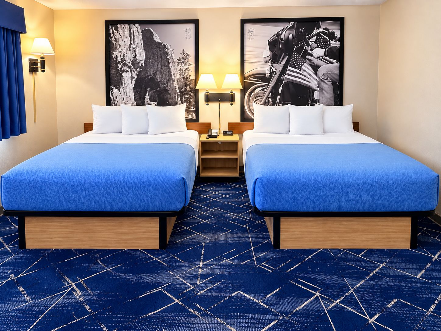 Une chambre d’hôtel avec deux lits, une moquette bleue et deux lampes fixées au mur.