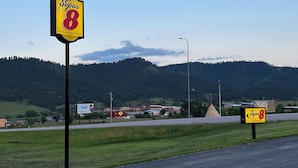 A Super 8 motel sign by Wyndham with a clear view of the surrounding landscape, including a road, grassy areas, and distant hills. - Super 8 by Wyndham Hot Springs (Hot Springs)