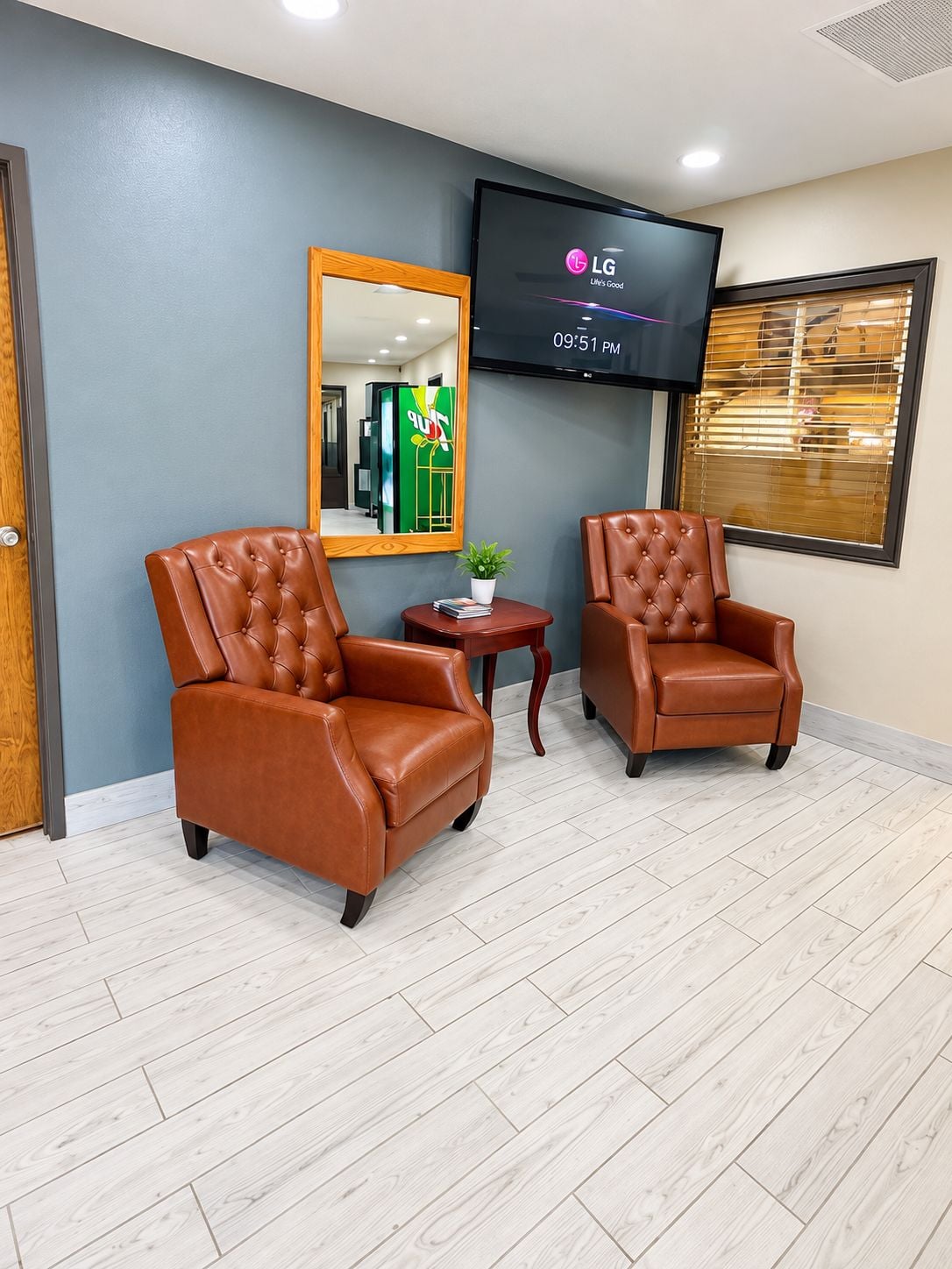 A room with two brown leather armchairs, a small table with a plant, and a flat-screen TV mounted on the wall displaying the LG logo.