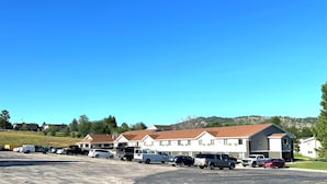 A parking lot with several vehicles, including cars and trucks, in front of a row of white buildings with brown roofs. - Super 8 by Wyndham Hot Springs (Hot Springs)