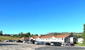 A parking lot with several vehicles, including cars and trucks, in front of a row of white buildings with brown roofs. - Super 8 by Wyndham Hot Springs (Hot Springs)