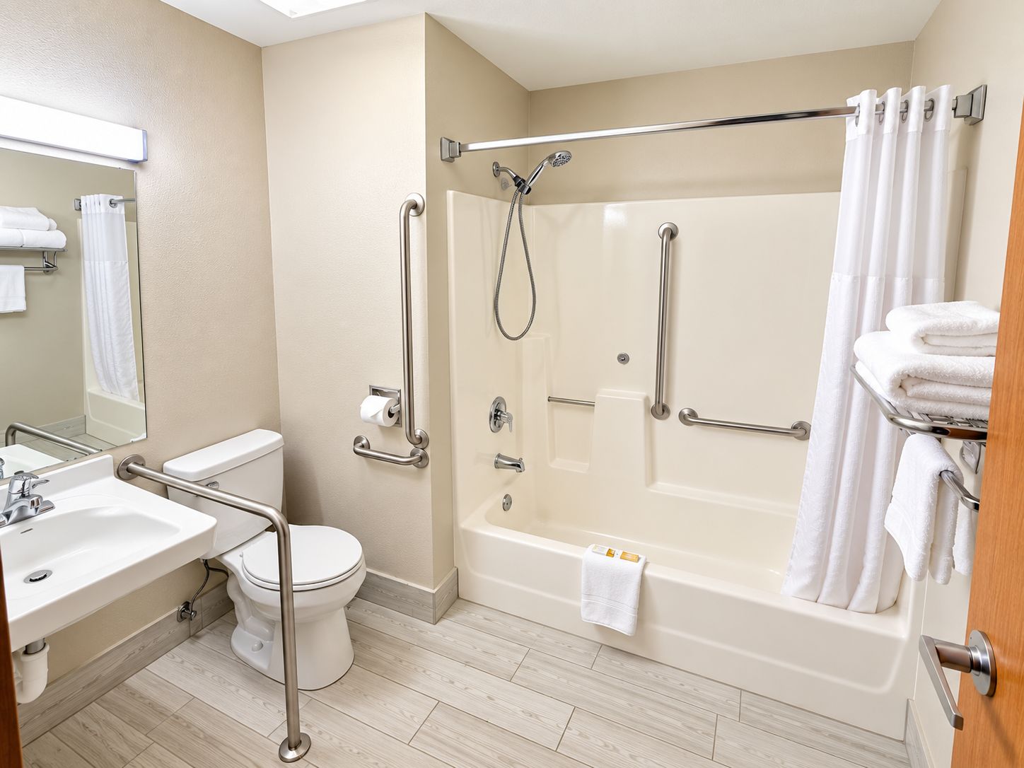 A bathroom with a bathtub, toilet, sink, and handrails.