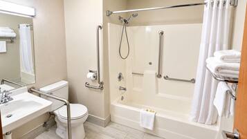 A bathroom with a bathtub, toilet, sink, and handrails.