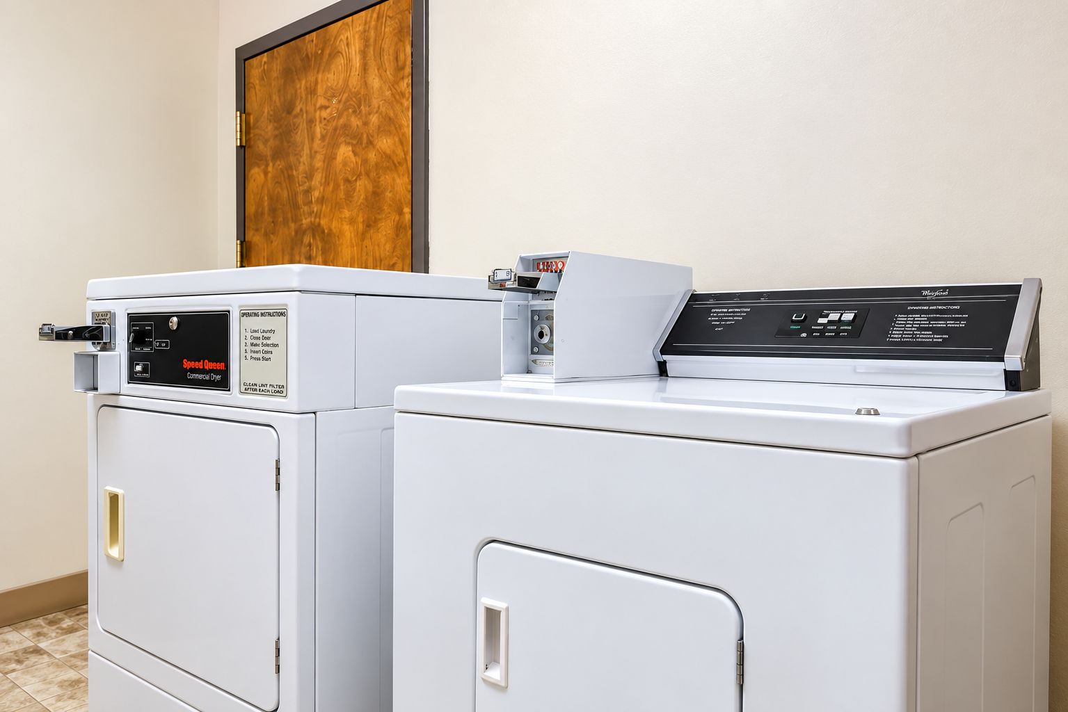 Two front-loading washers in a laundry room with a wooden door above.