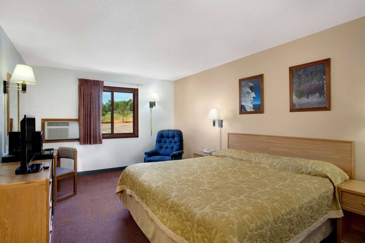 Een hotelkamer met een bed, een bureau met een computer, een stoel, een raam met gordijnen en twee wandlampen.